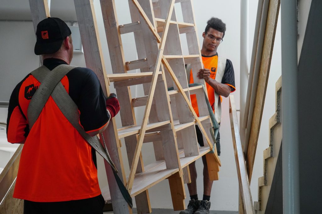 Yritysmuutto Helsinki. Kuvassa kaksi muuttotiimin jäsentä kantaa isoa hyllyä yrityksen tiloihin.